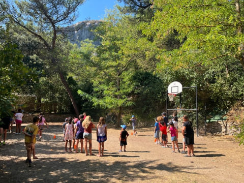Bambini giocano a basket all'aperto su un campeggio circondato da alberi a La Vallée Heureuse, Provenza, Francia.