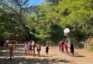 Children play basketball outdoors on a campsite surrounded by trees at La Vallée Heureuse in Provence, France.