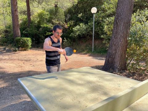Uomo che gioca a ping pong all'aperto in un campeggio circondato da alberi in Provenza-Alpi-Costa Azzurra, Francia.