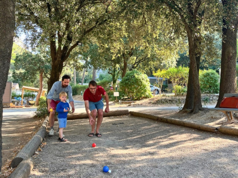 Due adulti e un bambino giocano a pétanque all’ombra degli alberi nel campeggio La Vallée Heureuse in Provenza.