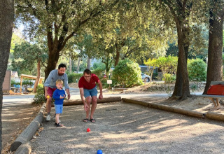 Due adulti e un bambino giocano a pétanque all’ombra degli alberi nel campeggio La Vallée Heureuse in Provenza.