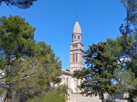 Historic stone bell tower rising among green trees under blue skies at La Vallée Heureuse campsite in Provence-Alpes-Côte d’Azur, France.