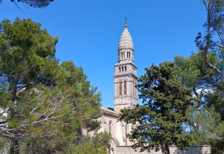 Historic stone bell tower rising among green trees under blue skies at La Vallée Heureuse campsite in Provence-Alpes-Côte d’Azur, France.
