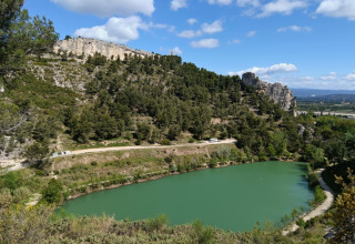 View of a green pond surrounded by forested hills near Orgon in Provence-Alpes-Côte d’Azur, France, under blue sky.