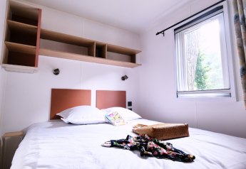 Schlafzimmer im Mobile Home Premium auf dem Campingplatz La Vallée Heureuse, großes Bett und Fenster.