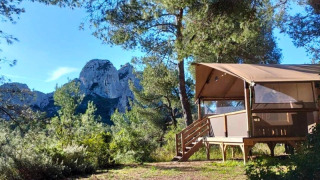 Tenda safari Premium Lodge tra i pini con vista sulle montagne e cielo azzurro, ideale per un soggiorno nella natura.