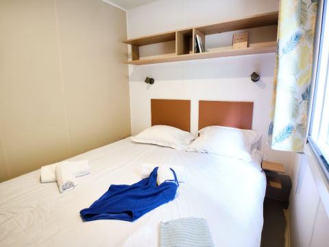 Schlafzimmer im Mobile Home Premium auf Campingplatz La Vallée Heureuse, Doppelbett, helles Fenster.