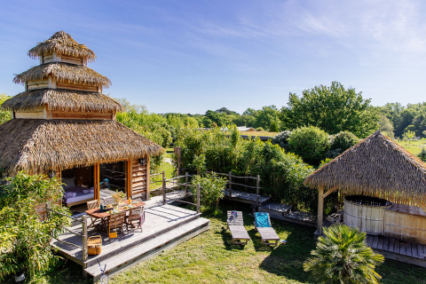 Økohytte med stråtag og træterrasse i Domaine EcÔtelia omgivet af grønne planter, Nouvelle-Aquitaine, Frankrig.