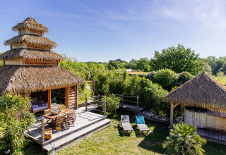 Cabane écologique au toit en chaume avec terrasse bois, Domaine EcÔtelia entouré de verdure, Nouvelle-Aquitaine, France.