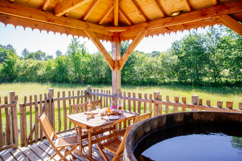 Zicht vanaf boomhut Temple perché in Domaine EcÔtelia, met houten terras, tafel, stoelen en hottub.