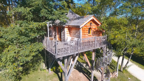 Træhytte på pæle blandt træer i Domaine EcÔtelia feriepark, Nouvelle-Aquitaine, Frankrig, set om dagen.