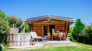 Blokhut Trappeur met spa, terras, ligstoelen en jacuzzi in groene natuur onder een blauwe hemel.