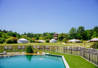 Udsigt over en naturlig swimmingpool og grønne telte i Domaine EcÔtelia feriepark, Nouvelle-Aquitaine, Frankrig.