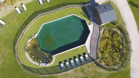 Luftfoto af en ottekantet pool med liggestole, træhegn og grønne områder ved Domaine EcÔtelia, Frankrig.
