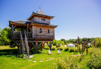 Baumhaus namens Log cabin Temple perché mit Spa, in grüner Natur, sonniger Himmel im Hintergrund.
