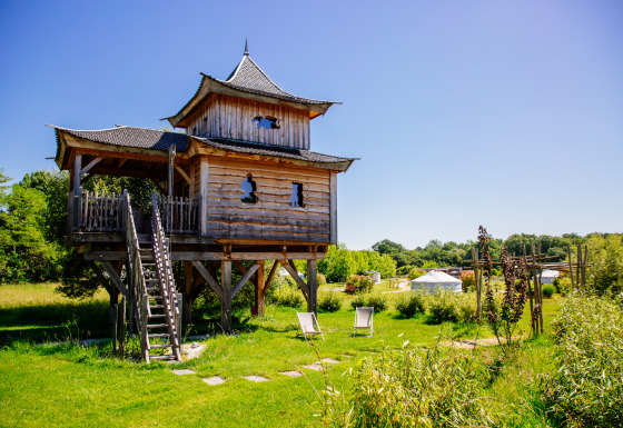 Cabane dans les arbres Temple perché avec spa, au milieu de la verdure sous un ciel bleu clair.