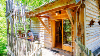Et billede af et hyggeligt træhus kaldet Treehouse Palombière med to personer, der sidder på terrassen.