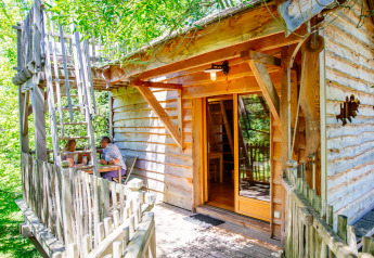 Foto von Treehouse Palombière, einem rustikalen Baumhaus mit zwei Personen, die auf der Veranda sitzen.