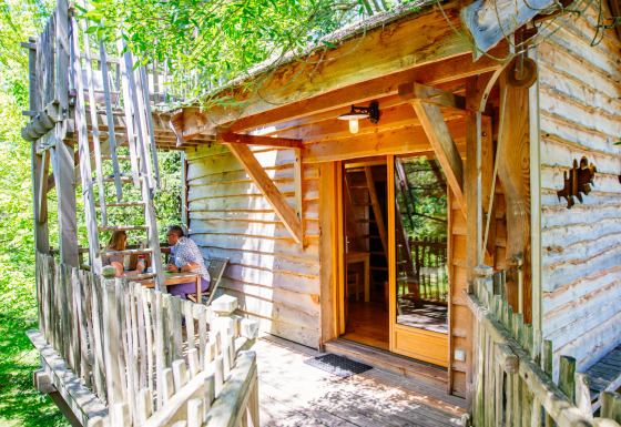 Foto della Treehouse Palombière, una casa sull’albero rustica con due persone sedute sul terrazzo.