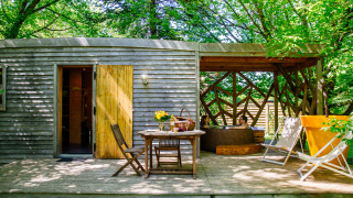 Houten terras aan een lodge met tafel, ligstoelen en twee personen in een bubbelbad omgeven door bomen.