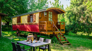 Bunte Zigeunerwagenhütte im Grünen mit gedecktem Frühstückstisch und Bäumen im Hintergrund.