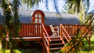 Gypsy wagon Viticole: Charming wooden cabin with a deck and chairs, nestled in a lush, green setting.