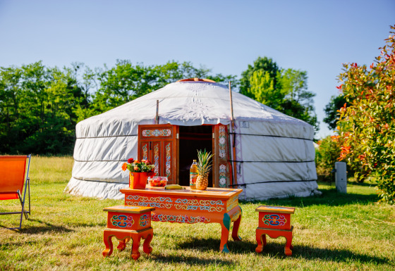 Yourte traditionnelle avec meubles peints colorés, fleurs et fruits à l’extérieur sur l’herbe ensoleillée.