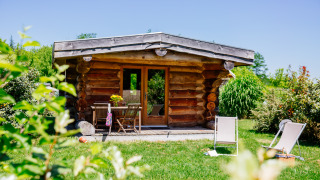 Casa de madera Trappeur en la naturaleza, césped verde, sillas de jardín y tumbonas al sol.