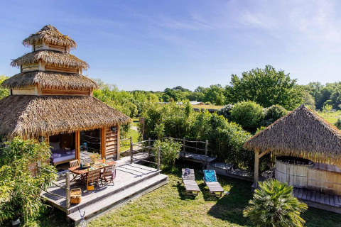 Maison nature de style indonésien avec spa, toit de chaume, terrasse en bois et jardin verdoyant.