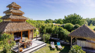 Indonesische Hütte mit Spa, Strohdach und Holzterrasse inmitten grüner Natur und Liegestühlen.