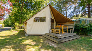 Tente safari Ecolodge avec terrasse en bois et coin repas extérieur, située dans un camping arboré.