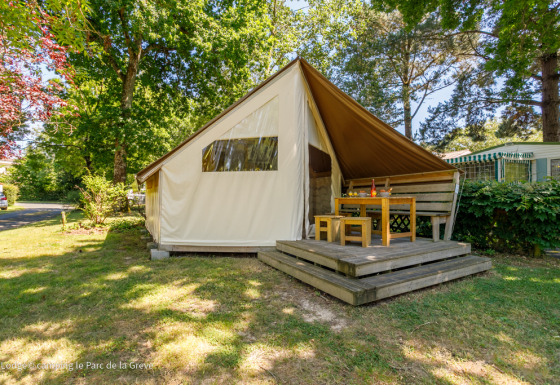 Tente safari Ecolodge avec terrasse en bois et coin repas extérieur, située dans un camping arboré.