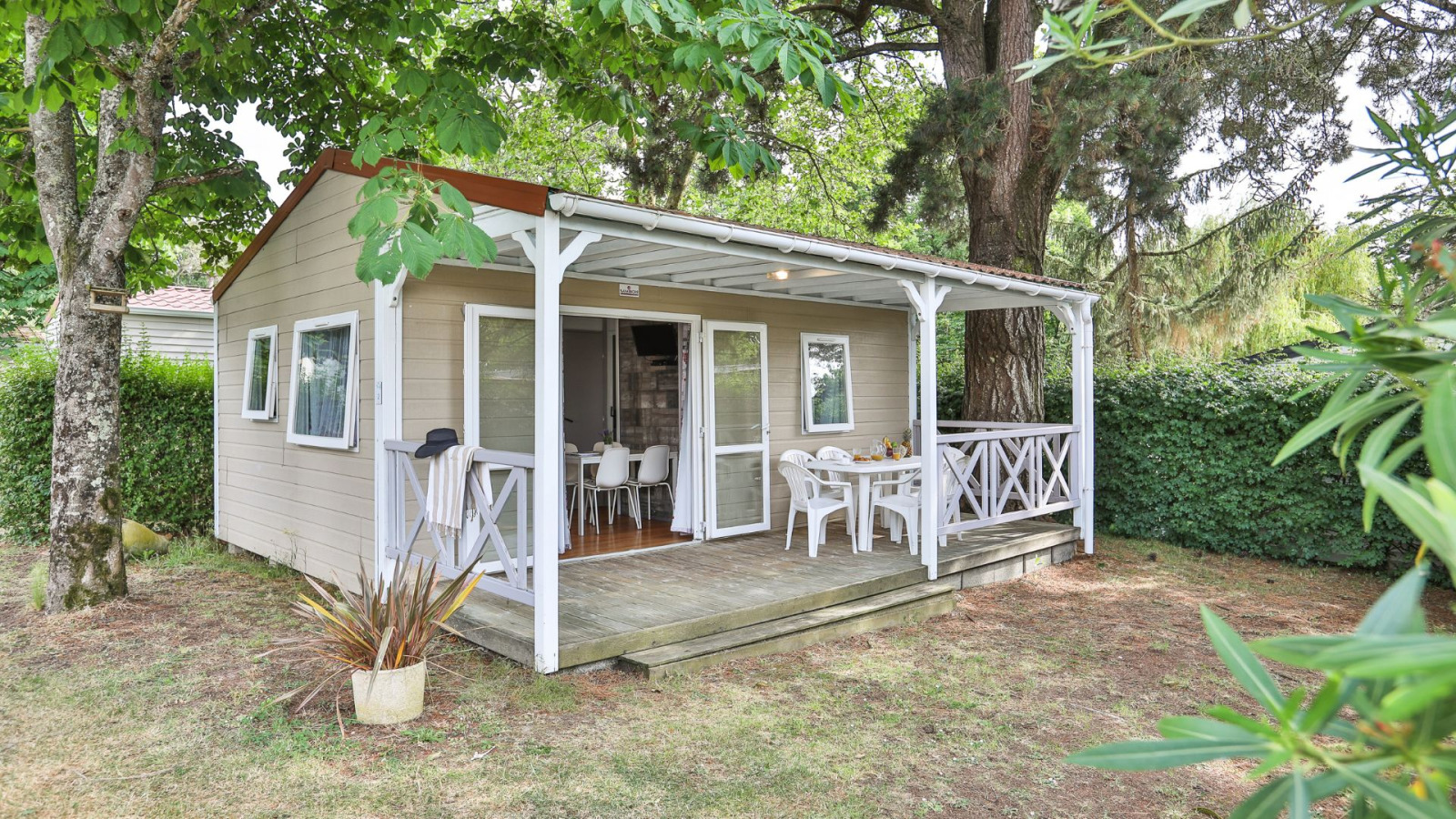 Buitenaanzicht van Relax Chalet 2 slaapkamers met overdekte veranda, witte stoelen en groene tuin.