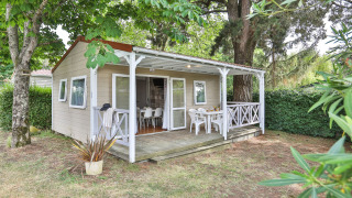 Buitenaanzicht van Relax Chalet 2 slaapkamers met overdekte veranda, witte stoelen en groene tuin.