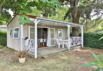 Vista exterior del Relax Chalet de 2 dormitorios con porche cubierto, sillas blancas y jardín verde.