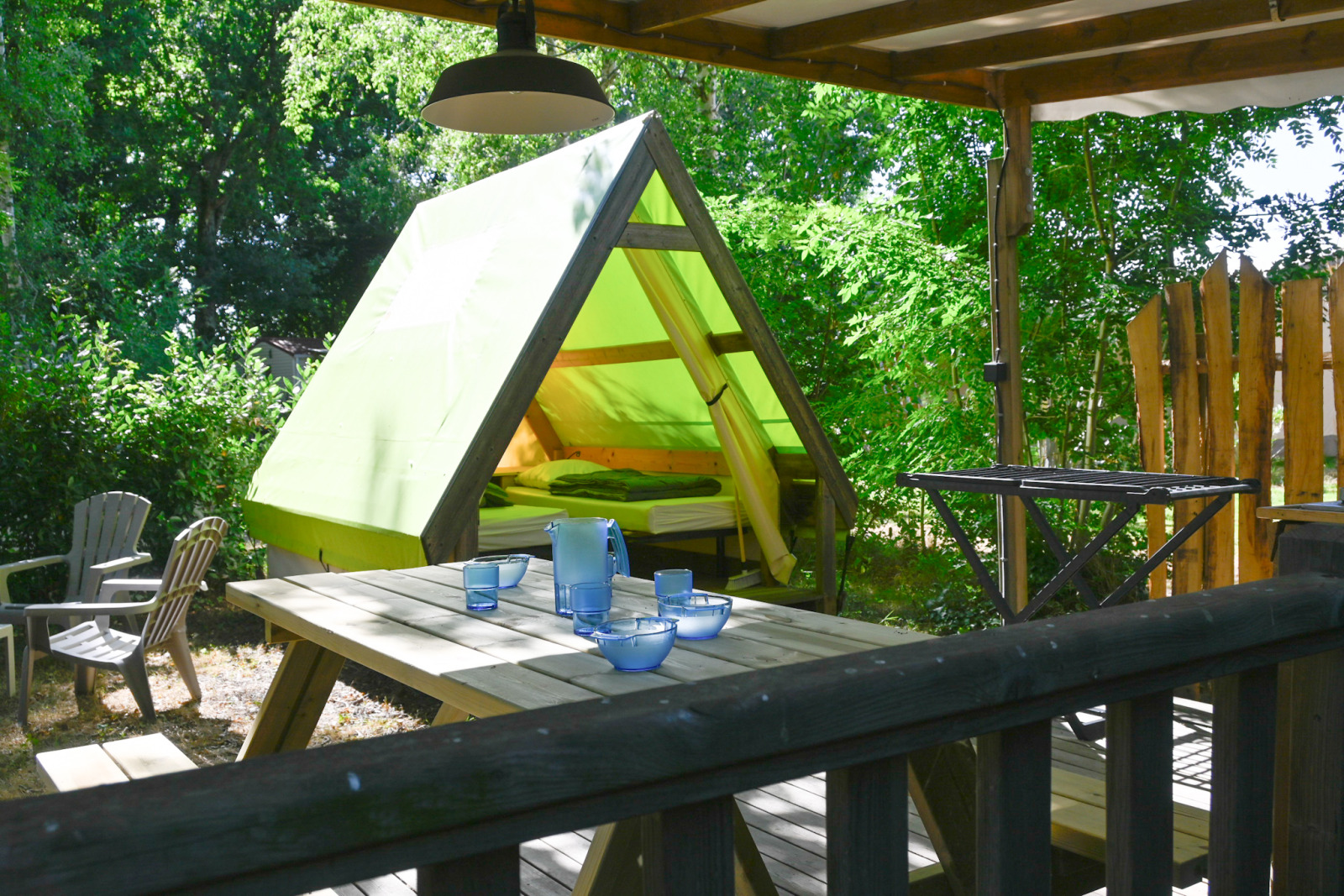Safari tent genaamd Backpackers tent met groene tentdoek, picknicktafel en stoelen op een overdekt terras.