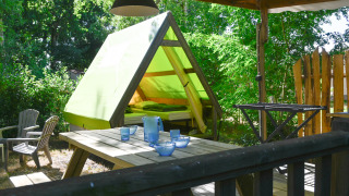 Backpackers tent safari telt med grøn teltdug, træterrasse, picnicbord og stole i naturrige omgivelser.