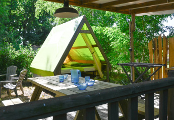 Backpackers tent safari telt med grøn teltdug, træterrasse, picnicbord og stole i naturrige omgivelser.