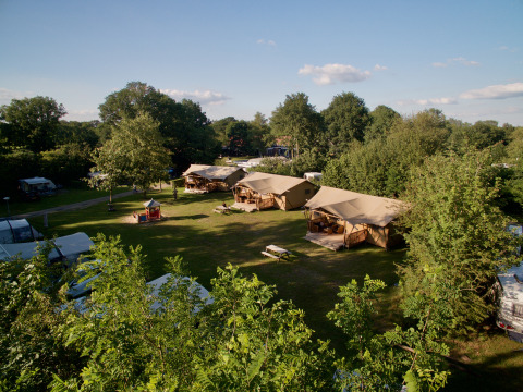 Vista aérea de la tienda Safari Appelgaard en un camping verde rodeado de árboles y cielo azul claro.