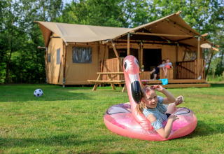 Girl playing on pink flamingo float outside Safari tent «Vogelkers» at Recreation park Kaps, Netherlands.