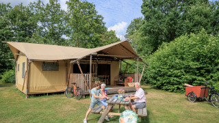 Family at picnic table outside safari tent 'Vogelkers' at Recreation park Kaps in the Netherlands, with bikes.