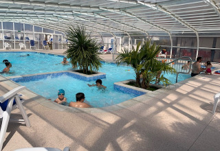 Piscina interna con palme e famiglie che si divertono al Flower Camping La Pointe du Talud in Bretagna, Francia.