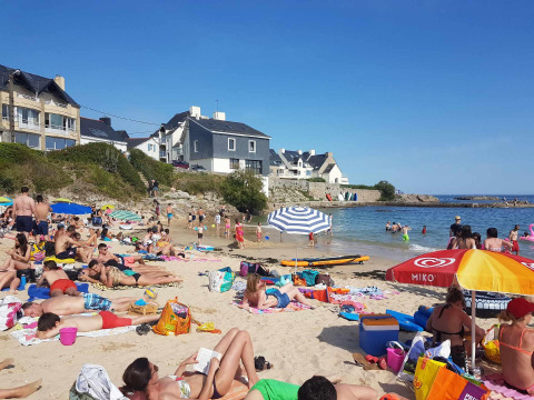 Travl strand i nærheden af Ploemeur i Bretagne, Frankrig, med folk der solbader, svømmer og farverige huse bagved.