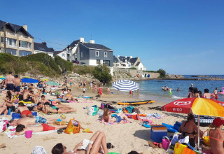 Spiaggia affollata vicino a Ploemeur, Bretagna, Francia, con bagnanti, ombrelloni colorati e case in sfondo.
