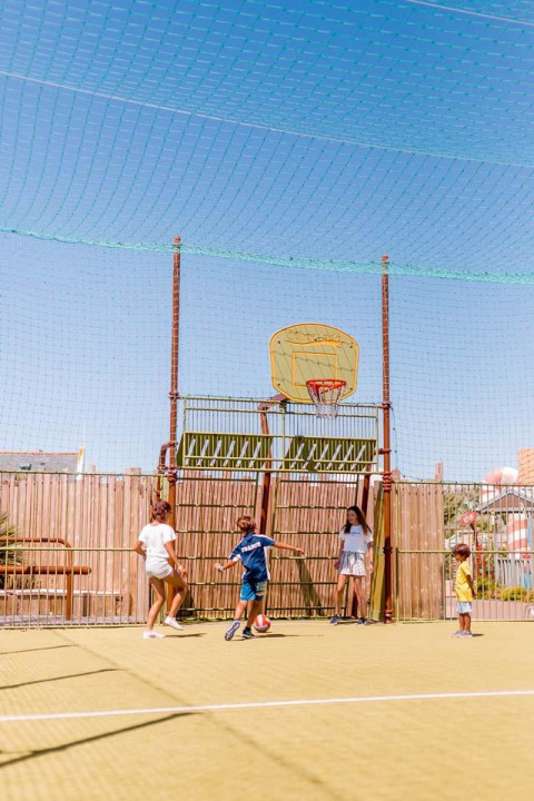 Bambini giocano a calcio sotto un canestro da basket su un campo esterno a Flower Camping La Pointe du Talud.