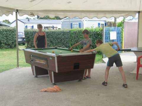 Kinder und eine Frau spielen Billard unter einem Zelt im Flower Camping La Pointe du Talud in der Bretagne.