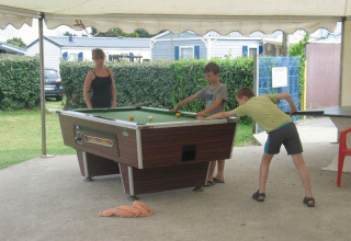 Kinder und eine Frau spielen Billard unter einem Zelt im Flower Camping La Pointe du Talud in der Bretagne.