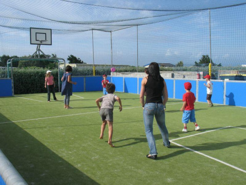 Kinder und Erwachsene spielen auf einem Outdoor-Sportfeld mit Netz im Flower Camping La Pointe du Talud, Bretagne.