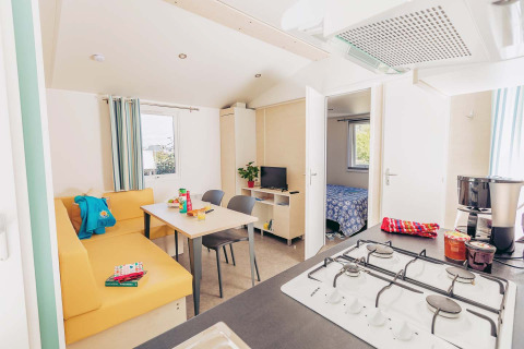Helles, modernes Mobilheim Comfort BAHIA mit Küche, Esstisch, Sofa und Blick ins Schlafzimmer.