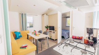 Luminoso e moderno Mobile home Comfort BAHIA con cucina, zona pranzo, divano e vista sulla camera.